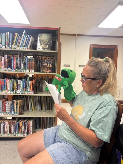A woman sitting in a chair holding a green puppet.